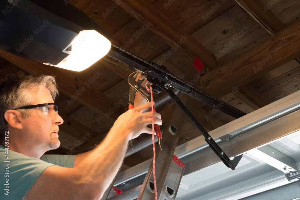 professional performing garage door opener installation duties on ladder