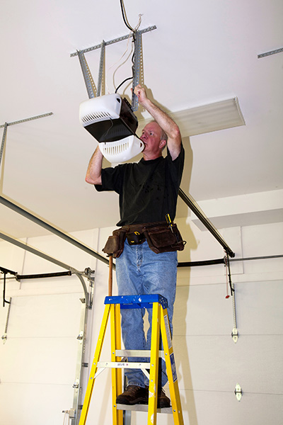 professional on yellow ladder and black shirt performing garage door opener installation duties