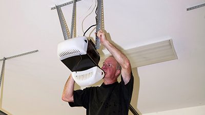 professional on yellow ladder and black shirt performing garage door opener installation duties